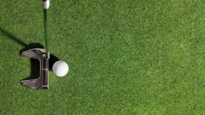 A photo of a putter and golf ball on a putting green